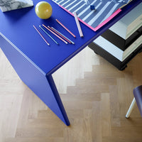 Vibrant purple desk with colorful pencils and striped paper on a light wooden floor, adding a playful touch to decor.