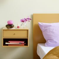 Yellow nightstand with pink and brown decor, lavender pillow, and soft pastel accents for a vibrant bedroom aesthetic.