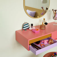 Stylish vanity in pink, orange, and lavender hues with a green and white striped purse and chic accessories.