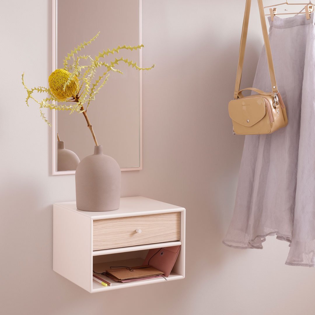Minimalist white wall shelf with natural wood drawer, soft gray skirt, yellow vase, and bright green foliage accents.