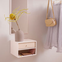 Minimalist white wall shelf with natural wood drawer, soft gray skirt, yellow vase, and bright green foliage accents.