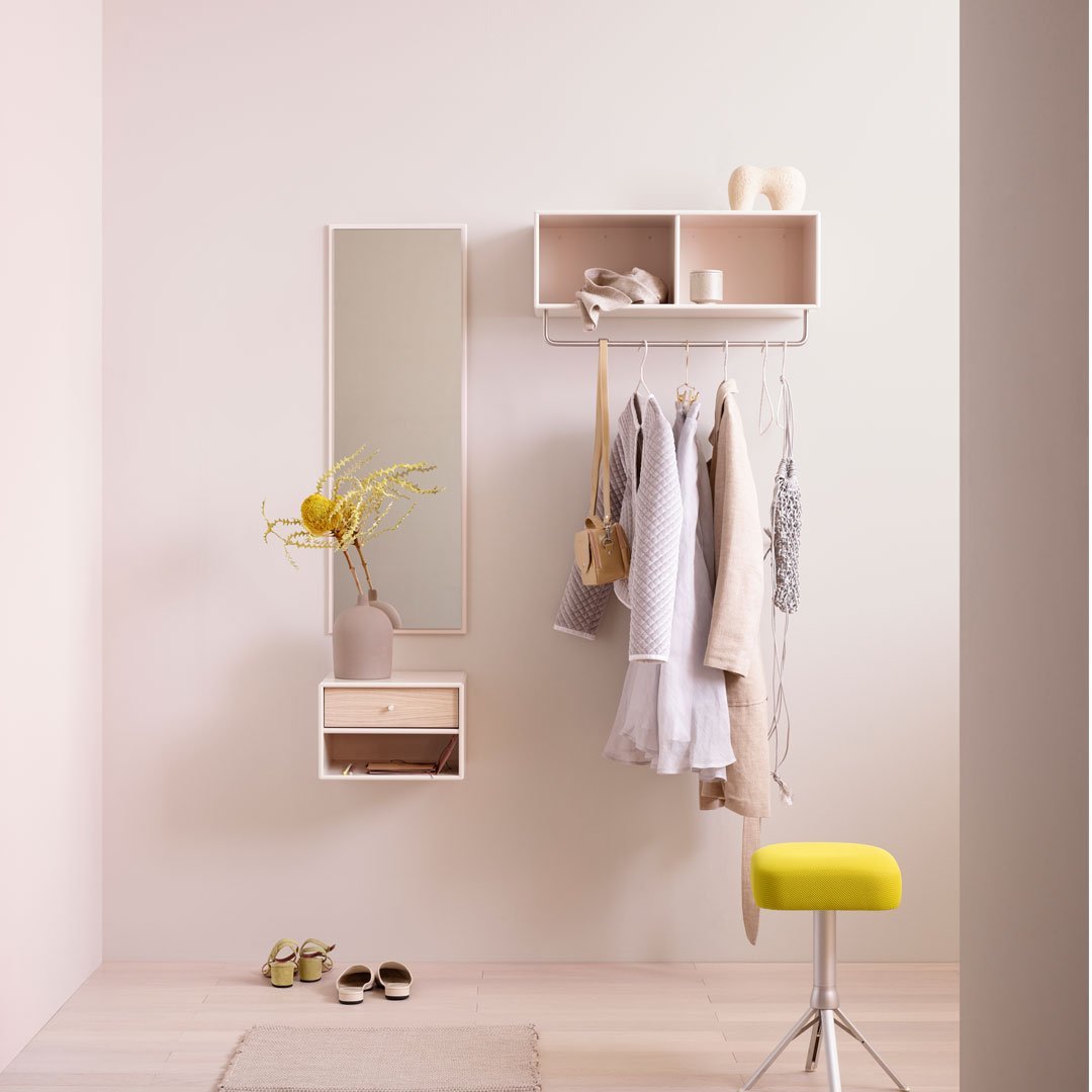 Light pink walls with beige accents, a yellow stool, and light gray clothing create a soft, modern aesthetic.