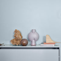Collection of natural textures and colors: beige, lavender, earthy tones, and soft wood against a pale blue backdrop.