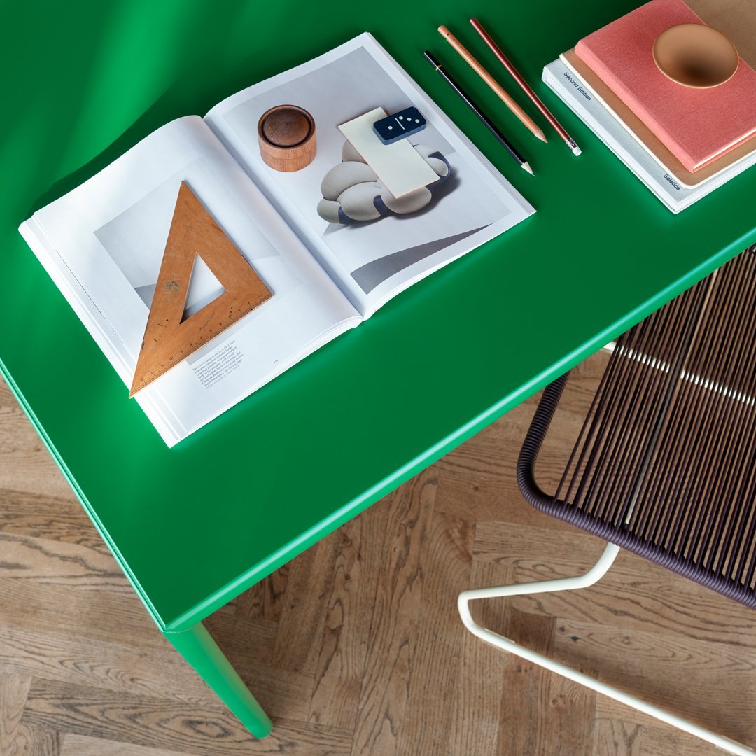 Bright green table with a glossy finish, wooden ruler, and colorful stationery on top, against a warm wooden floor.