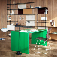 Modern green desk with sleek lines against a warm wood backdrop and contrasting geometric patterned shelves.