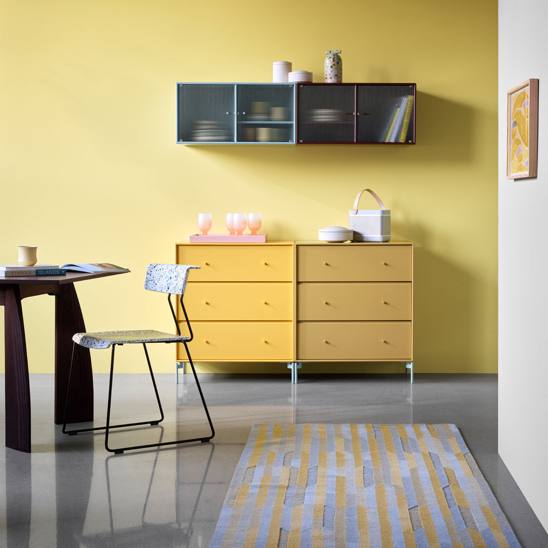 Stylish yellow dresser and chair with a patterned rug featuring light blue and cream stripes against a bright yellow wall.