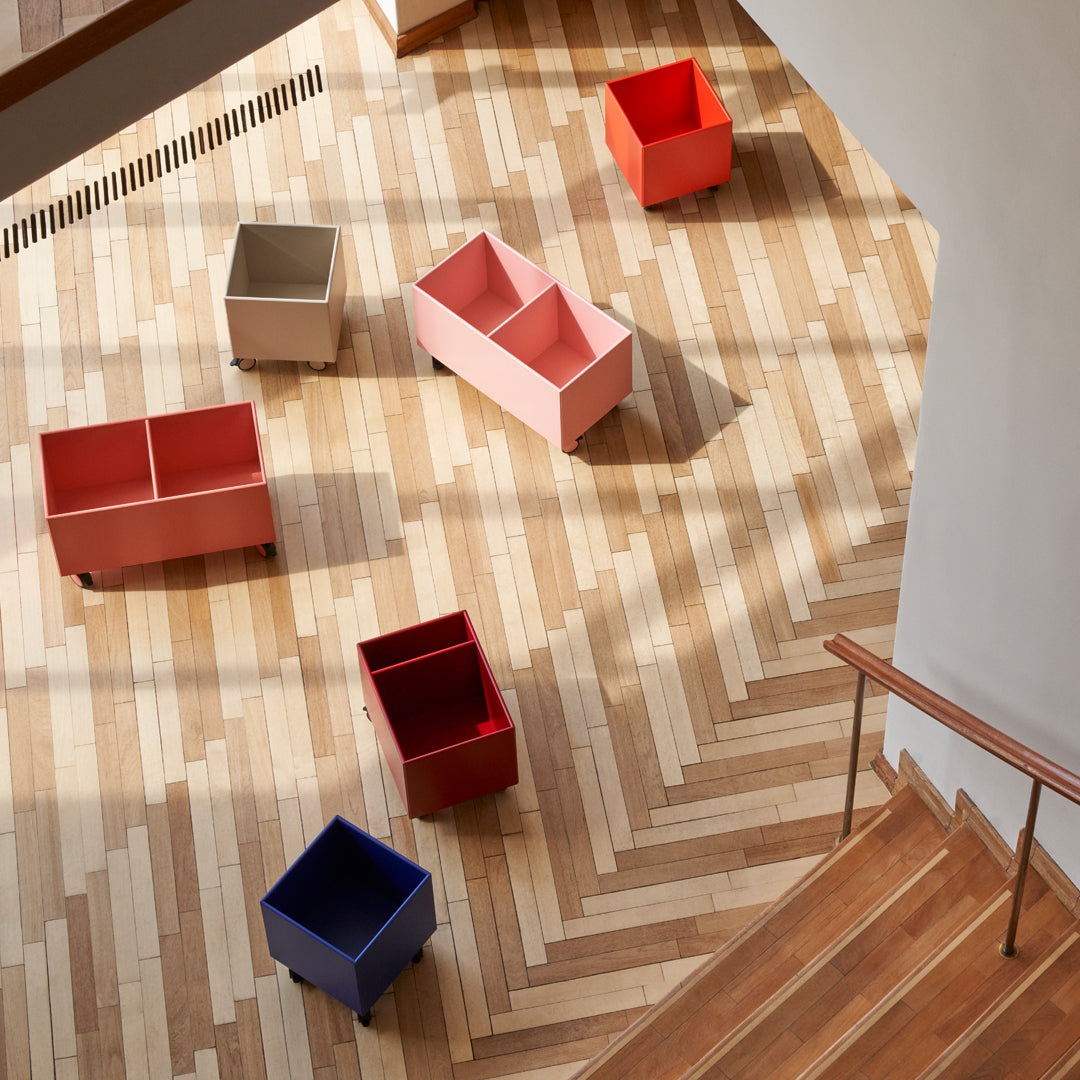 Colorful storage bins in pink, red, gray, and blue arranged on a geometric wooden floor with natural patterns.