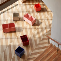 Colorful storage bins in pink, red, gray, and blue arranged on a geometric wooden floor with natural patterns.