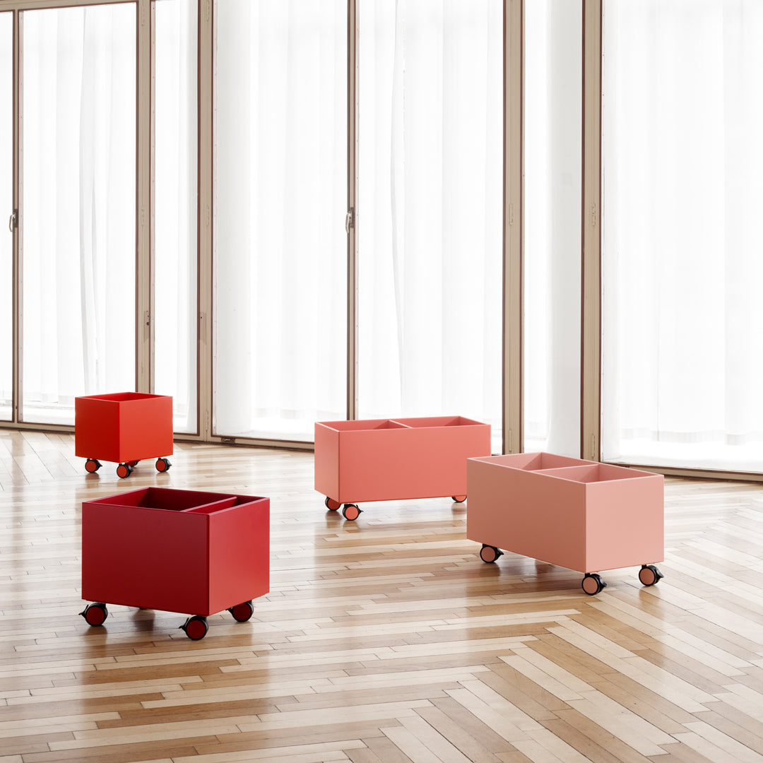 Red and blush pink storage bins on wheels, showcased on a wooden floor with natural light.