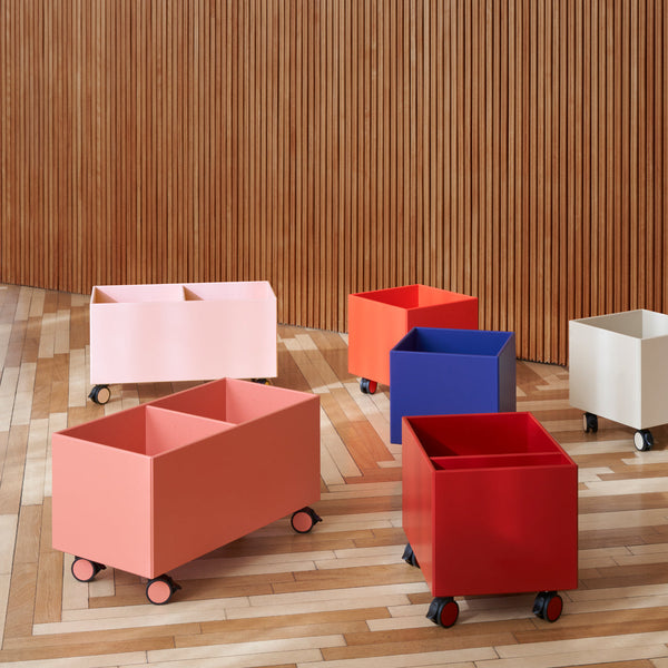 Colorful rolling storage bins in peach, red, blue, pink, and cream against a wooden backdrop.