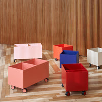 Colorful rolling storage bins in pink, coral, red, blue, and white, arranged on a wooden floor.