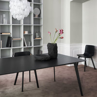 Black modern table, gray shelving, soft pink carpet, and black chair with a textured black vase and pink flowers.
