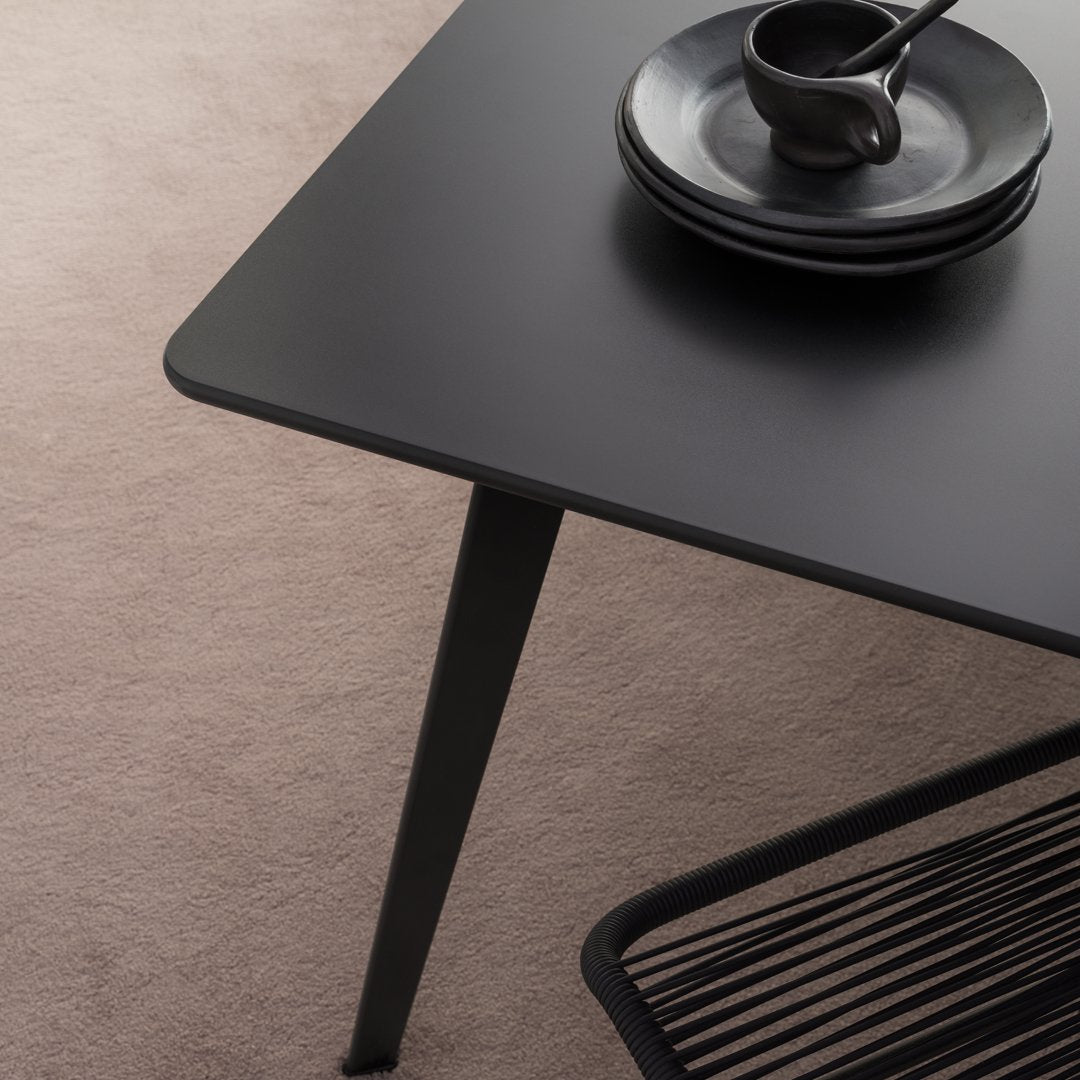Black matte dining table with sleek lines, paired with dark ceramic plates on a soft beige rug.