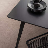 Black matte dining table with sleek lines, paired with dark ceramic plates on a soft beige rug.