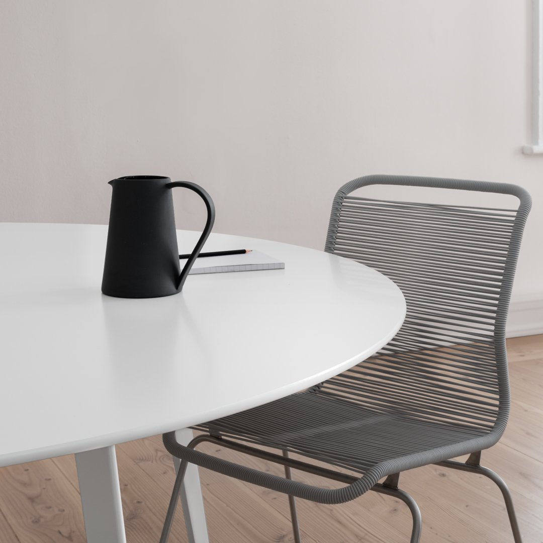 Black pitcher on a white table with a gray chair and soft wood flooring, creating a modern, minimalistic aesthetic.