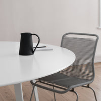 Black pitcher on a white table with a gray chair and soft wood flooring, creating a modern, minimalistic aesthetic.