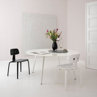 Modern dining room with a round white table, black and white chairs, pastel pink walls, and geometric art.
