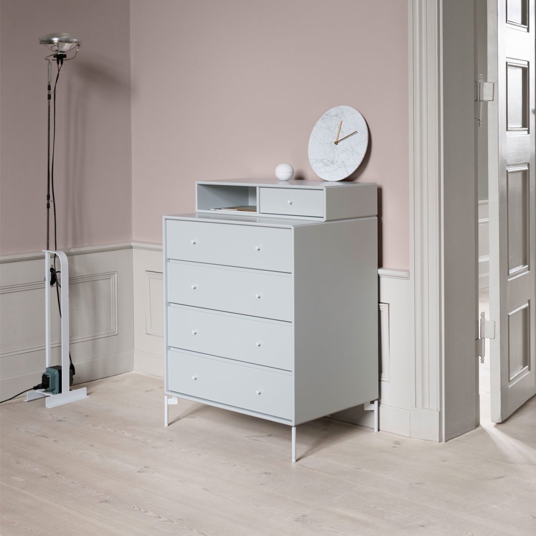 Light gray dresser against a soft pink wall, complemented by a marble clock and white accents. Minimalist design.