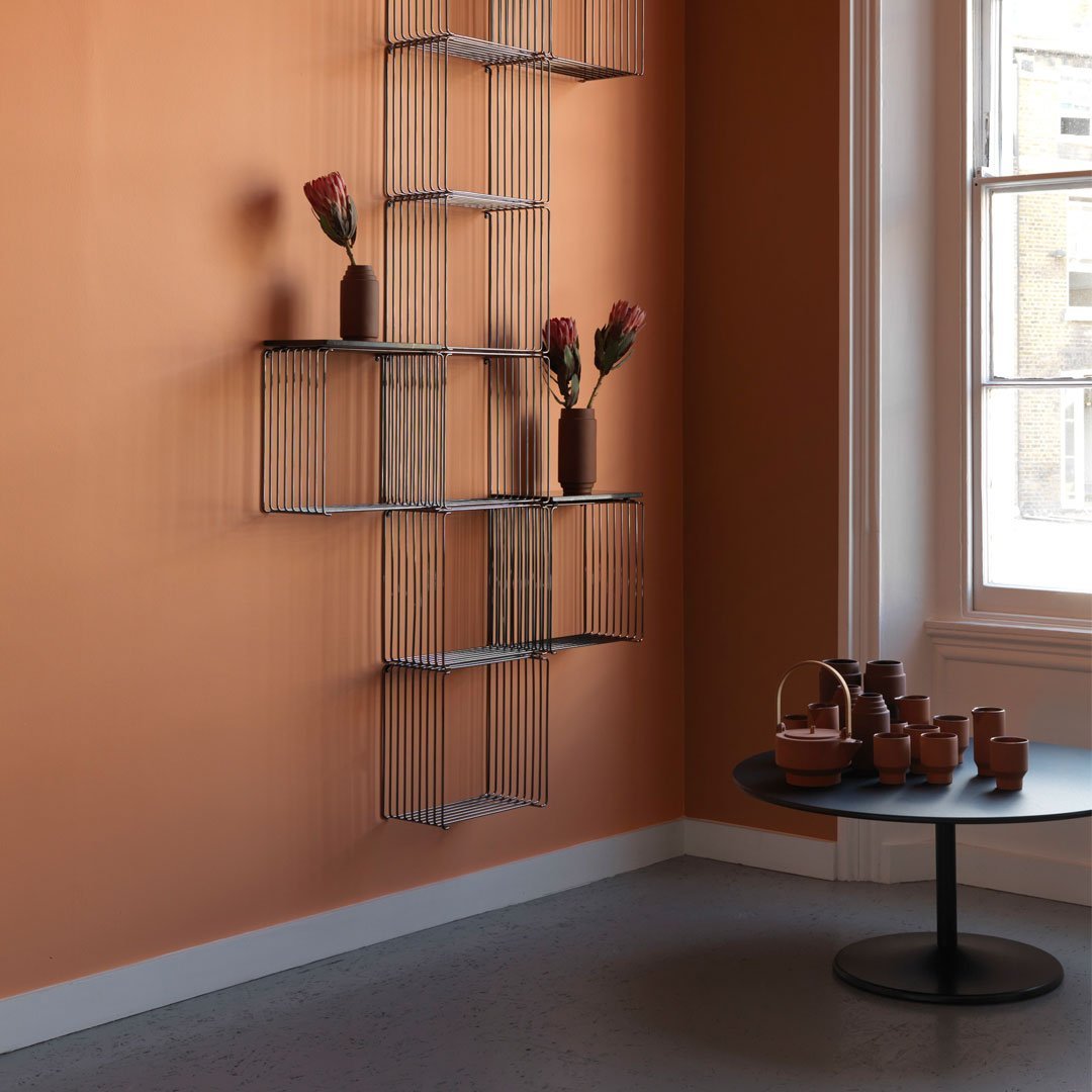 "Stylish shelving unit against a warm orange wall, featuring earthy tones and minimalist patterns with decorative vases."