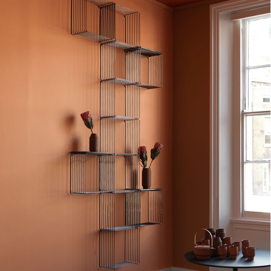 Geometric wire shelving in black against an earthy orange wall with accent vases and terracotta colors.