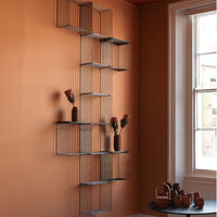 Geometric wire shelving in black against an earthy orange wall with accent vases and terracotta colors.