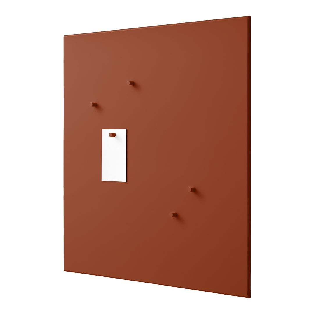 Rust-colored wall panel with a smooth matte finish and contrasting white rectangular tag. Features four small pegs.