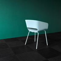 Light blue ribbed chair against a deep green wall and textured black tile floor, creating a modern color contrast.