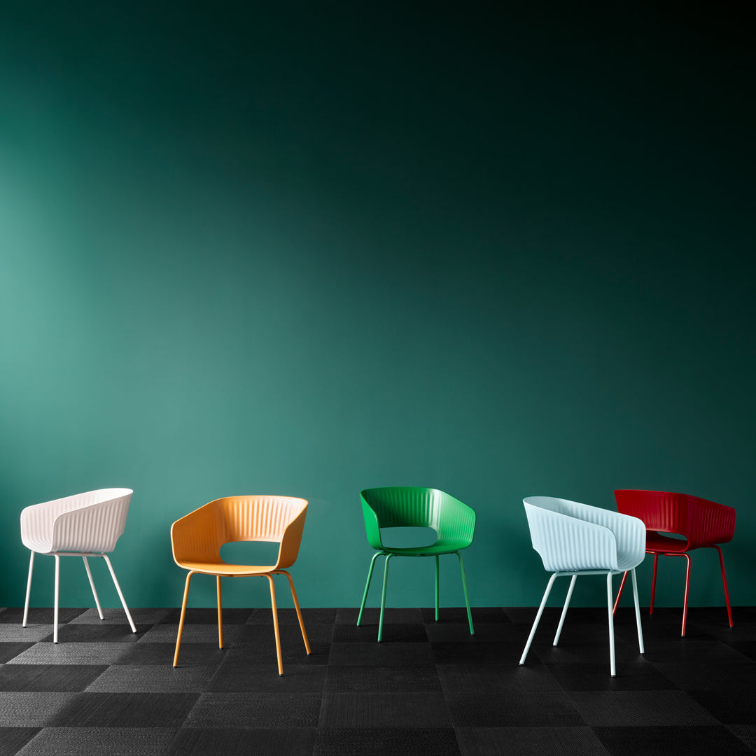 Colorful modern chairs in white, orange, green, light blue, and red against a teal background and black flooring.