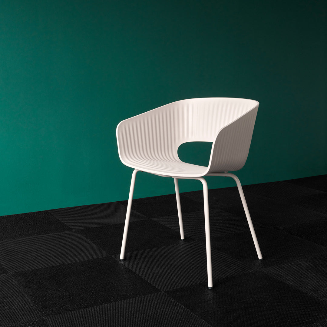 White ribbed chair against a deep teal wall and textured black flooring. Modern, minimalistic design.