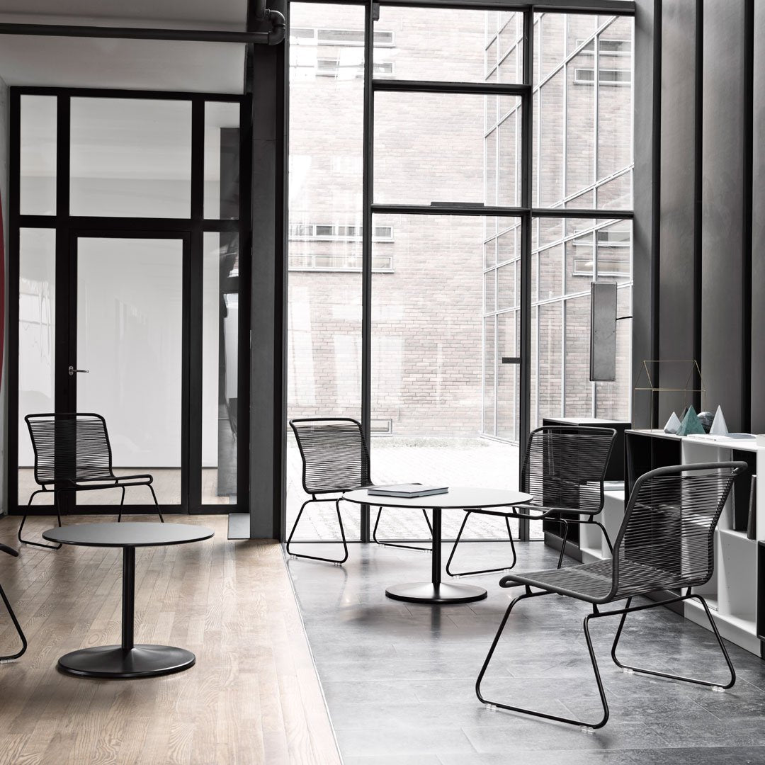 "Minimalist black wire chairs and table, contrasted against light wood and sleek dark flooring in a modern space."
