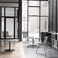 "Minimalist black wire chairs and table, contrasted against light wood and sleek dark flooring in a modern space."