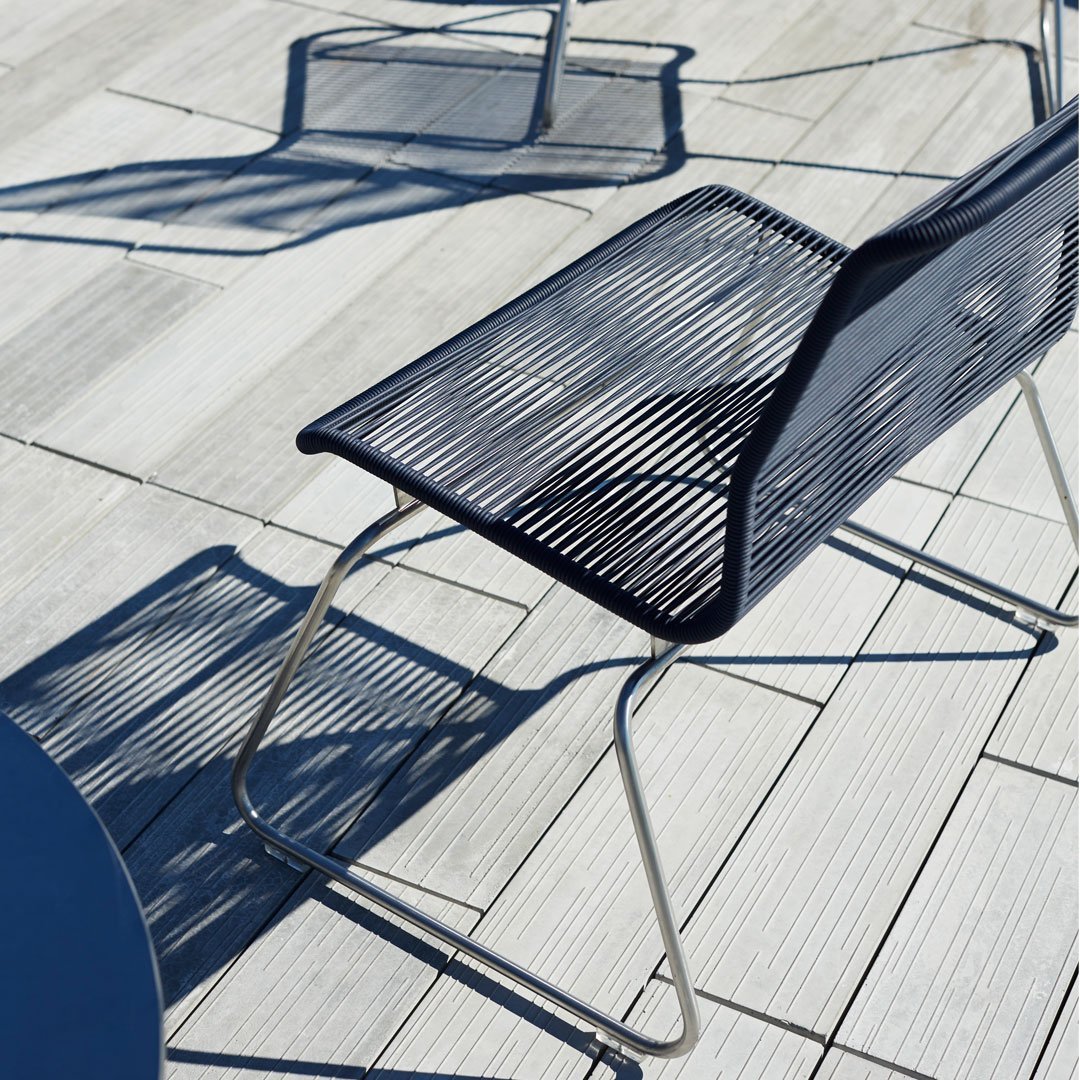 Navy blue striped chair on a light wooden deck, casting geometric shadows. Modern and sleek design.