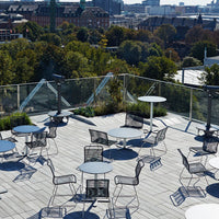 "Outdoor rooftop space featuring gray mesh chairs and round tables against a lush green backdrop."