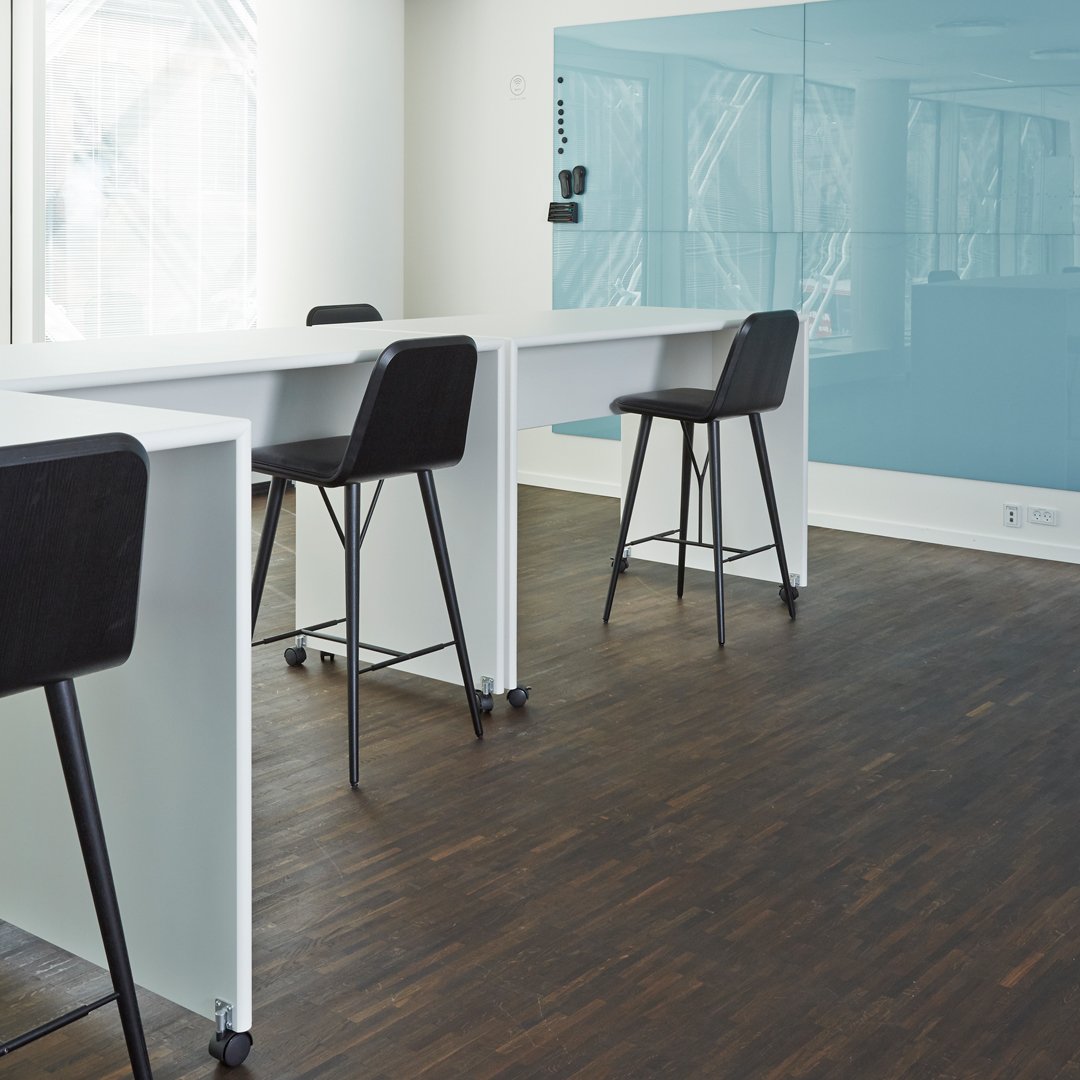Modern office setting with black chairs, white tables, and a soft blue wall, accented by dark wood flooring.