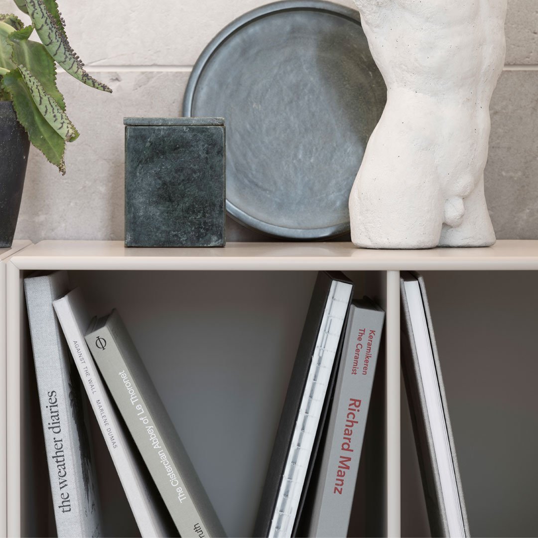 Stylish gray and green decor pieces with neutral books on a light shelf, set against a textured beige background.