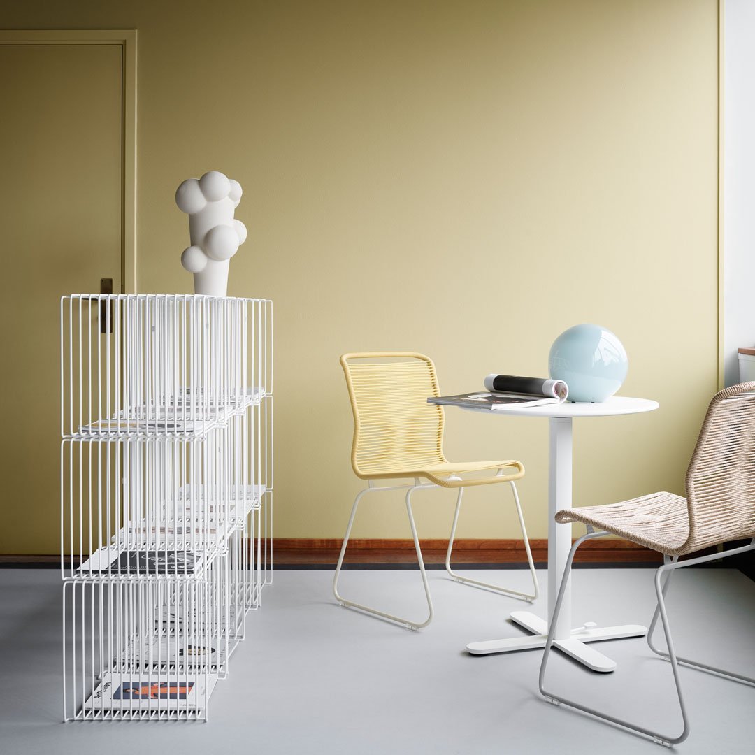 Modern interior with yellow and white chairs, a white wire shelf, and a light blue decorative sphere against a soft yellow wall.