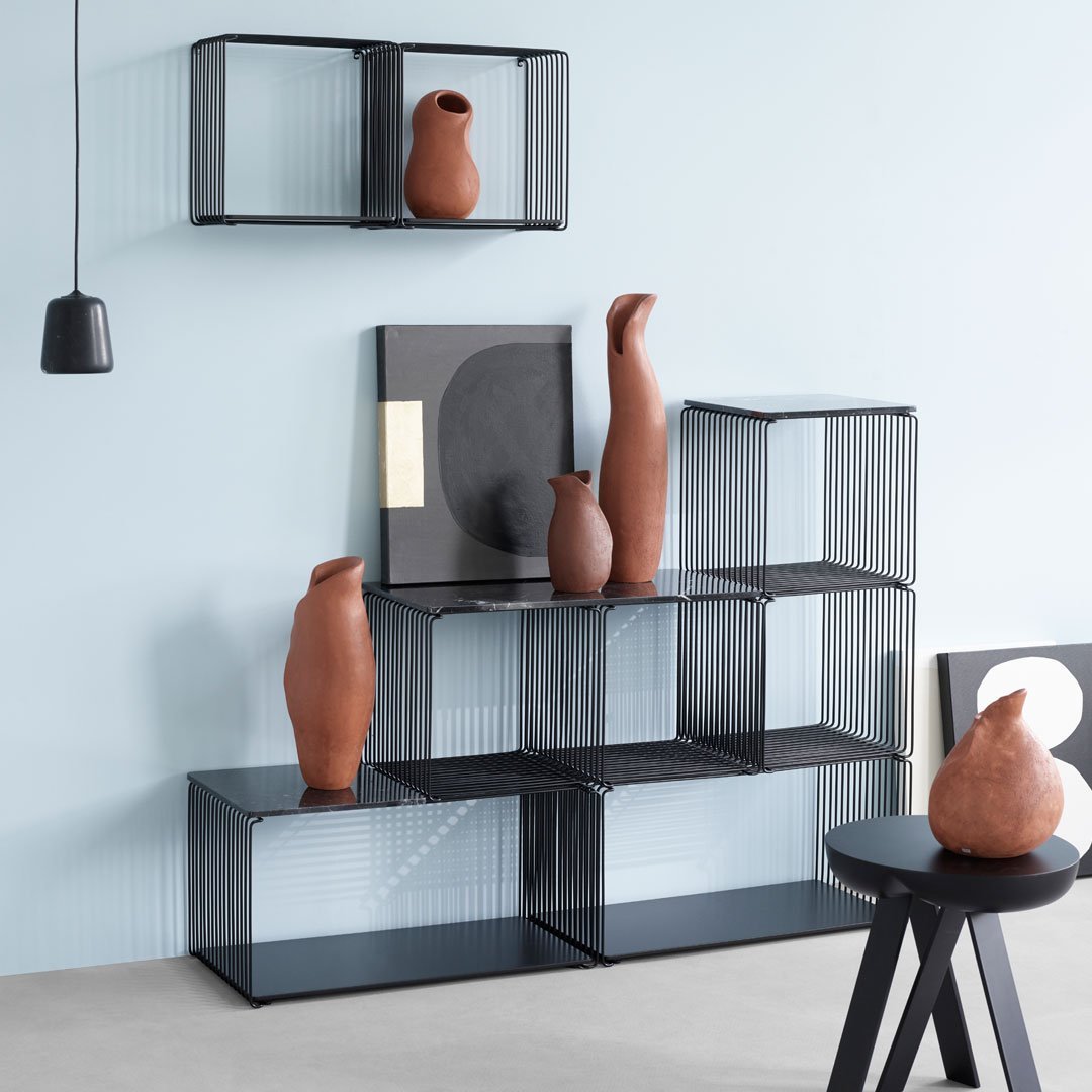 Black wire shelves with terracotta vases against a light blue wall, featuring geometric black and white patterns.