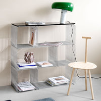 Modern wire shelving unit in silver with a sleek black top and accented by a green lamp and natural wooden chair.
