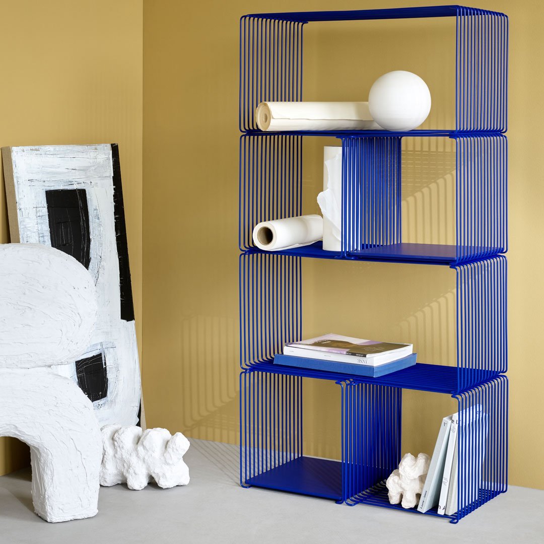 Blue wire shelving unit against a warm yellow background, featuring sleek lines and modern geometric patterns.