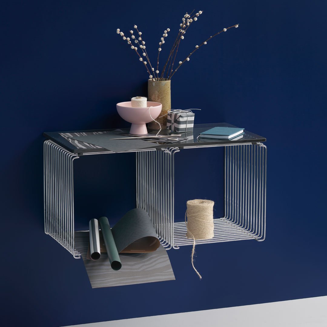Modern wire shelf in sleek black, accented by soft pink, green, and gray decorative items against a deep blue wall.
