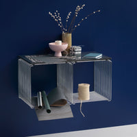 Modern wire shelf in sleek black, accented by soft pink, green, and gray decorative items against a deep blue wall.