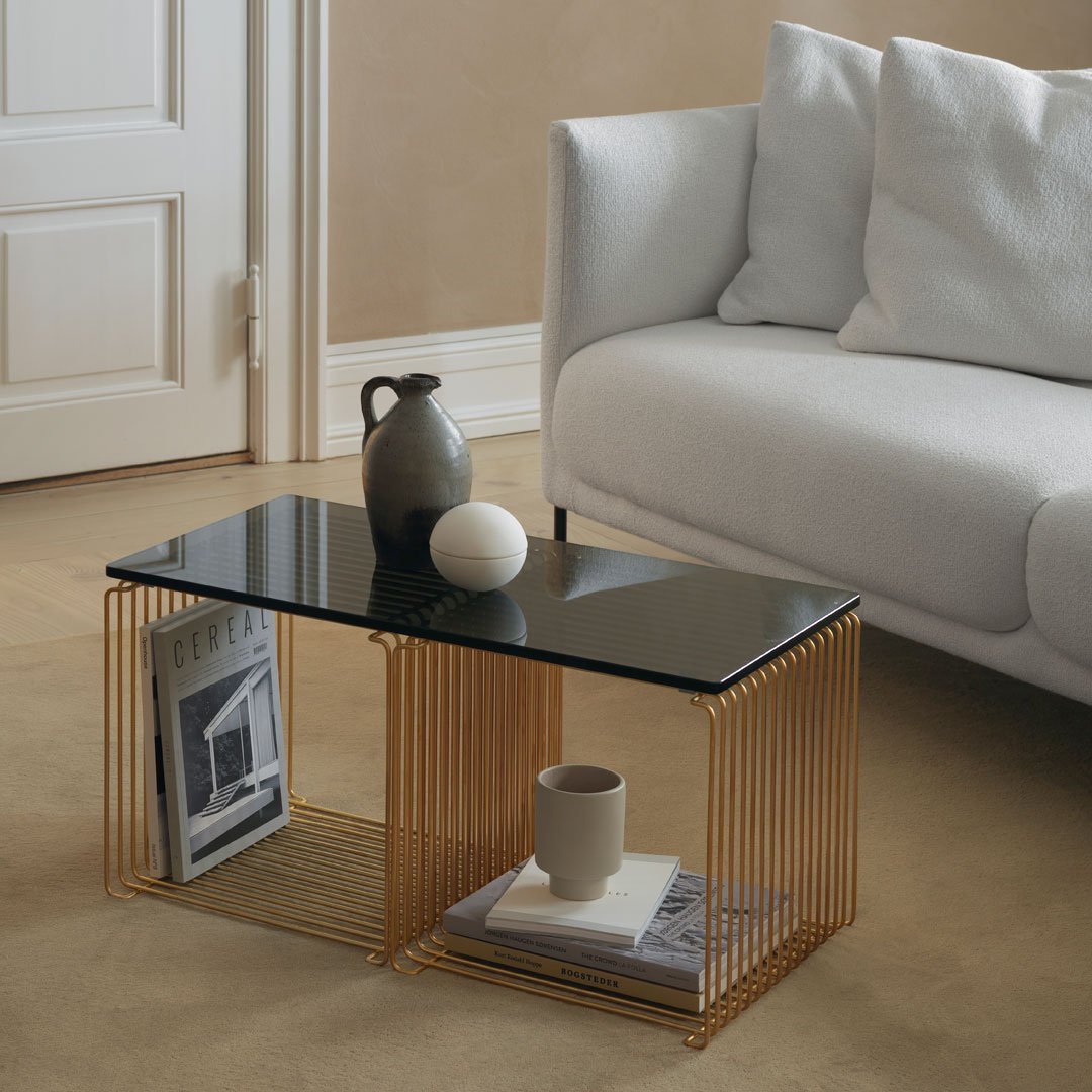 Modern black glass coffee table with gold wire frame, complemented by neutral-toned decor and soft textures.