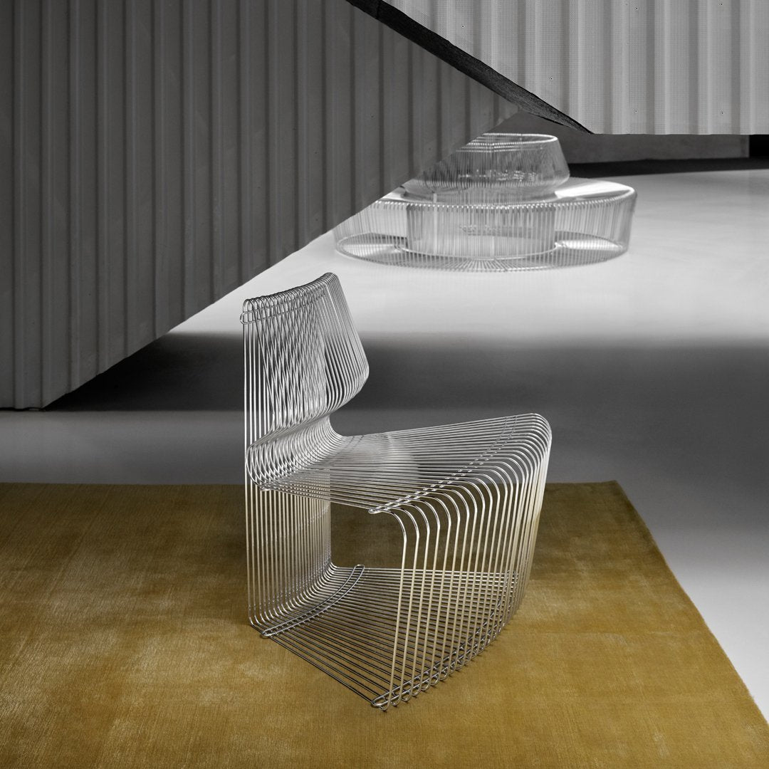 Clear acrylic chair with sleek, transparent lines against a soft golden rug and geometric backdrop.