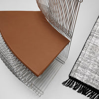 Brown leather seat cushion on a silver wire chair beside a textured black and white patterned rug.