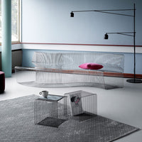 Modern wire sofa in silver with a vibrant pink pillow, paired with black accent tables on a textured gray rug.