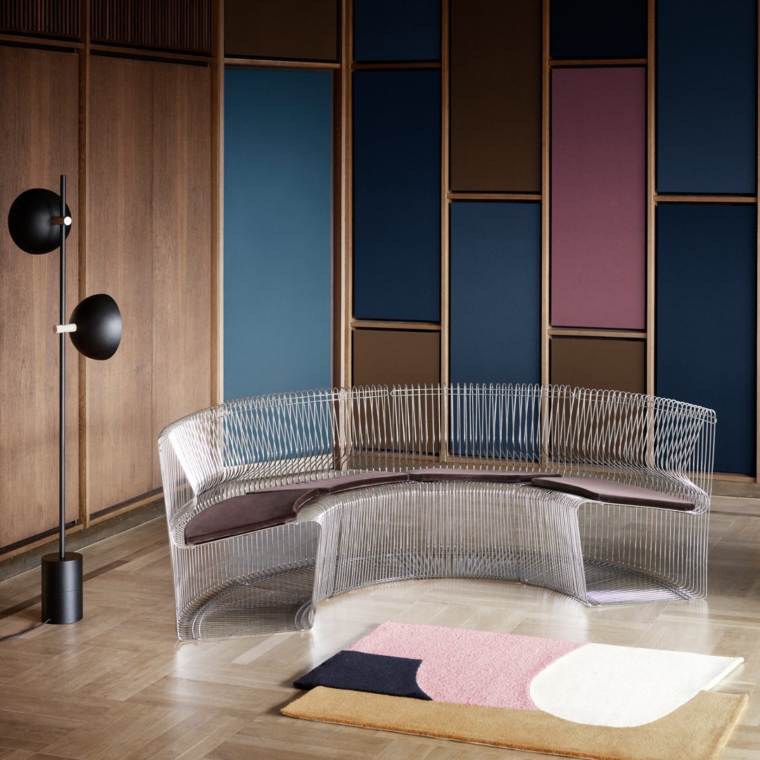 Transparent curved sofa with a dark brown cushion, set against multicolored walls in deep blue and soft pink tones.