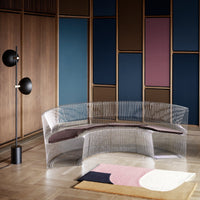 Transparent curved sofa with a dark brown cushion, set against multicolored walls in deep blue and soft pink tones.