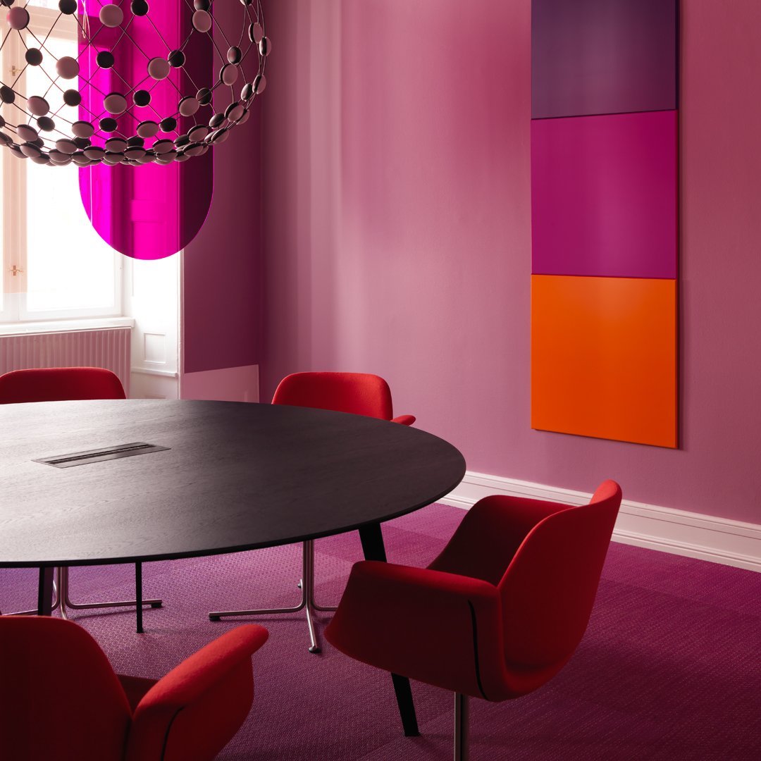 Modern meeting room featuring vibrant pink walls, red chairs, and bold orange and purple art pieces.
