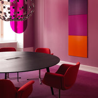 Modern meeting room featuring vibrant pink walls, red chairs, and bold orange and purple art pieces.