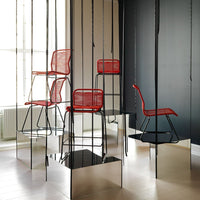 Red wire chairs with sleek black frames, surrounded by reflective surfaces and minimalistic decor.